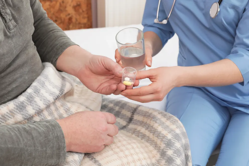Pflegekraft reicht einer Patientin Tabletten und ein Glas Wasser